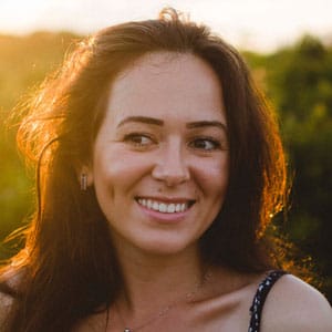 Close-up portrait of a woman with long dark hair smiling at the camera in natural light.