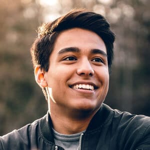 A young man with dark hair smiling while wearing a jacket outdoors.